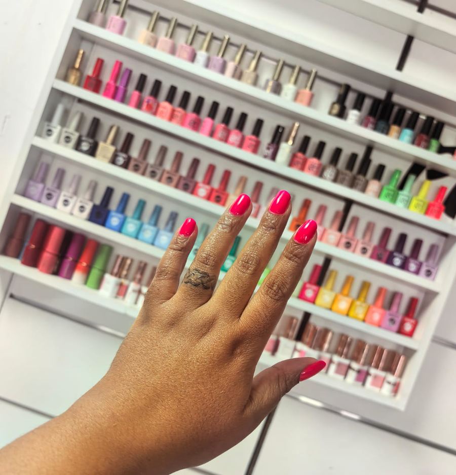 Bright pink gel manicure in front of the Rose Beauty Spa gel polish wall
